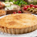 Chicken pie with cottage cheese, tomatoes, onion and olives on wooden table and white plate.